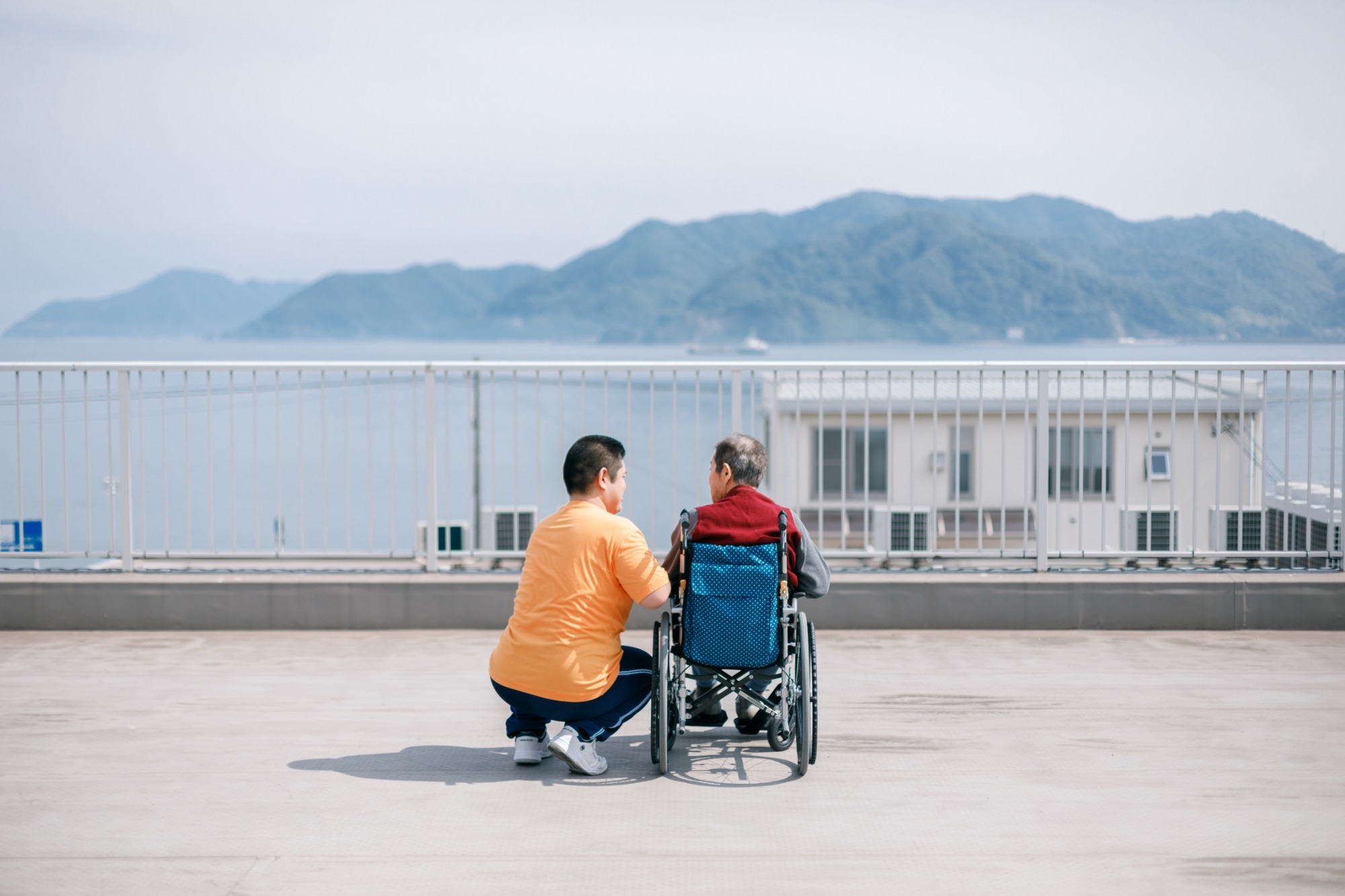 介護職員が車椅子利用者とテラスで交流する様子。山々が見える景観の良い屋上空間での活動風景